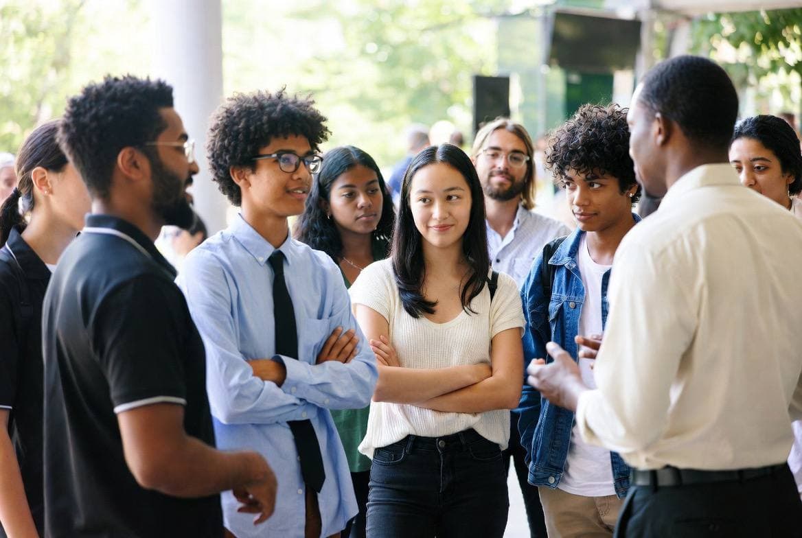 A group of young participants in conversation with a program staff member during an outdoor event